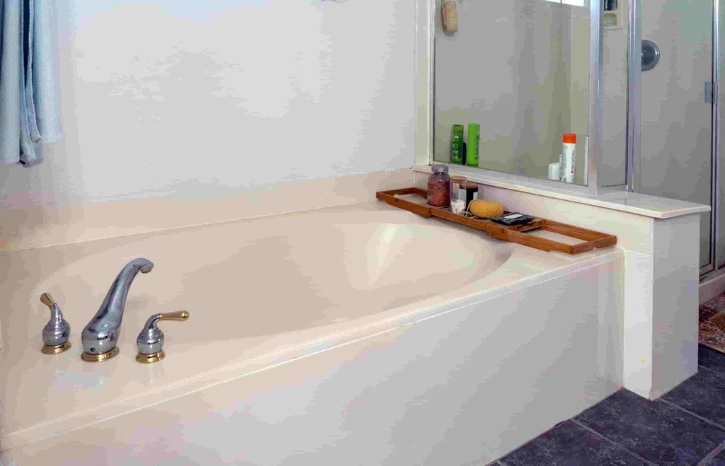 A white bathtub with a wooden tray on it and two faucets.