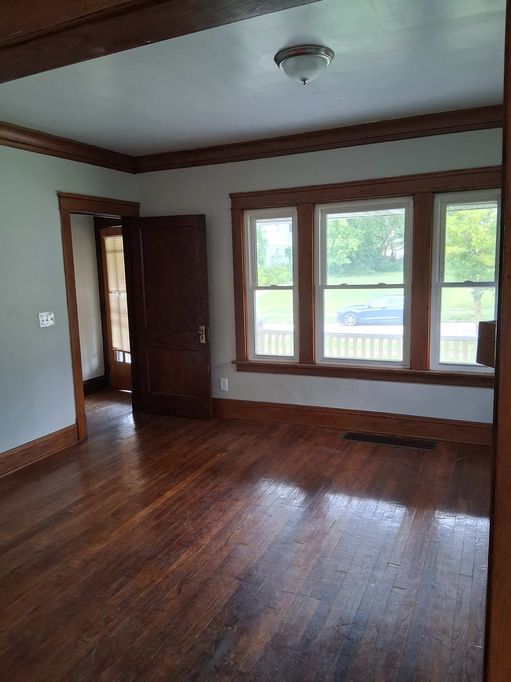 A room with wooden floors and a window overlooking a car.