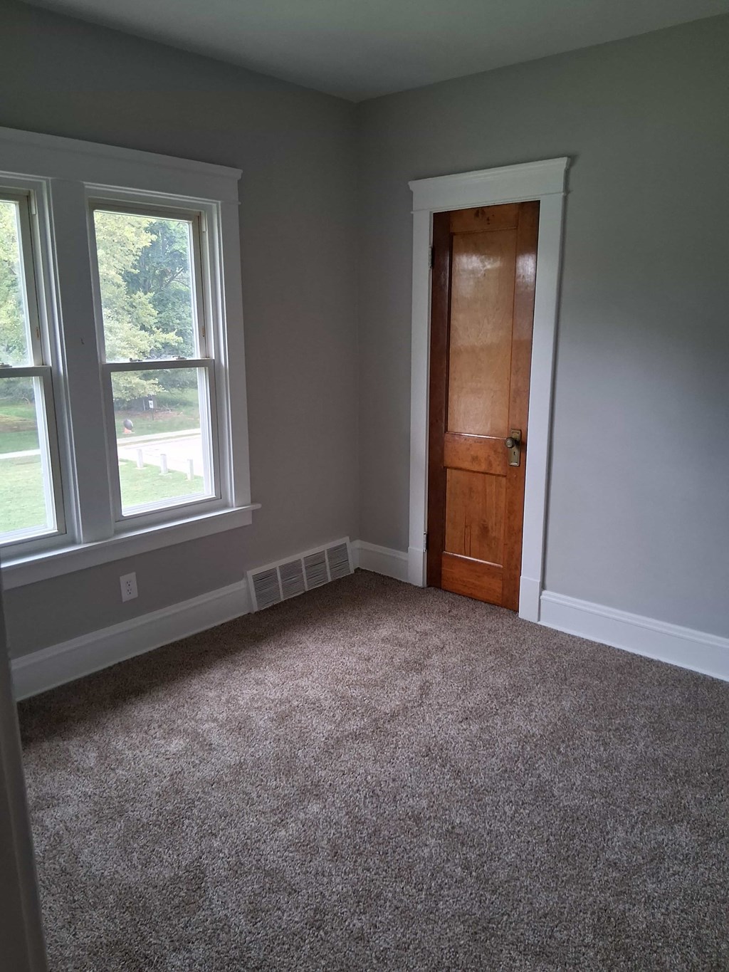 A room with a carpeted floor, a door, and a window.