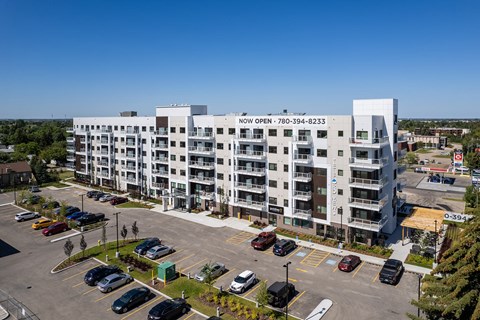 A large white building with the words "NOW OPEN" on the side is surrounded by a parking lot with many cars.