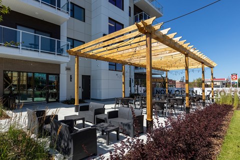 A wooden pergola is in front of a white building.