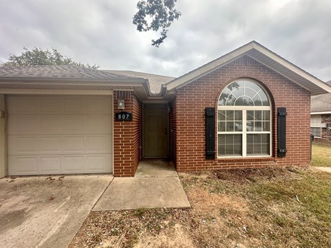A brick house with a white garage door and a window with black shutters.