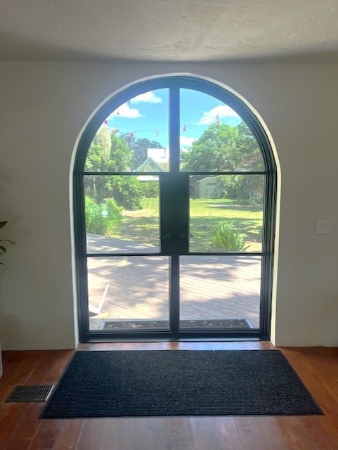 A black mat is on the wooden floor in front of a glass door.