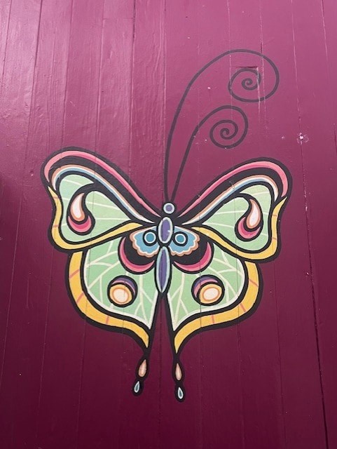 A butterfly with multi-colored wings is painted on a wooden surface.