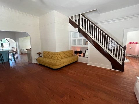 A living room with a yellow sofa and a wooden staircase.