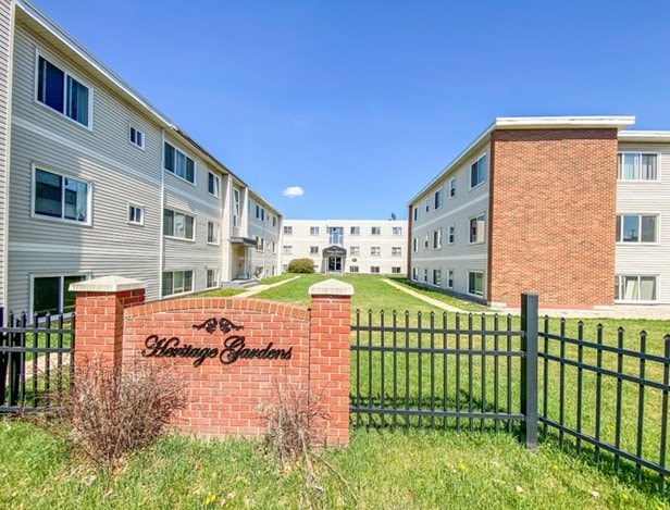 A brick sign that says "Whispering Gardens" is in front of a black fence.