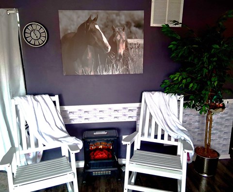 Two white chairs are in front of a purple wall with a framed picture of a horse.