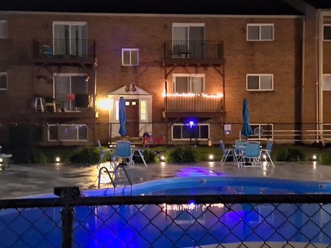 A pool in front of a building with lights on.