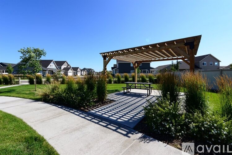 A sunny day at a park with a pavement, a bench and a pergola.