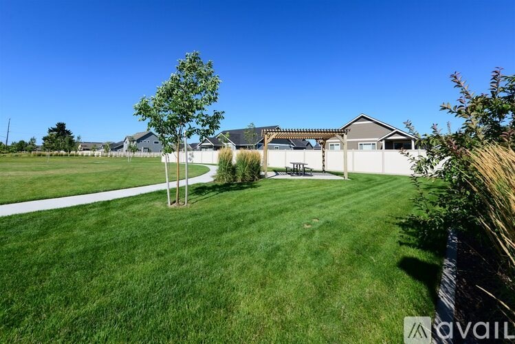 A grassy field with a house and a tree in the background.