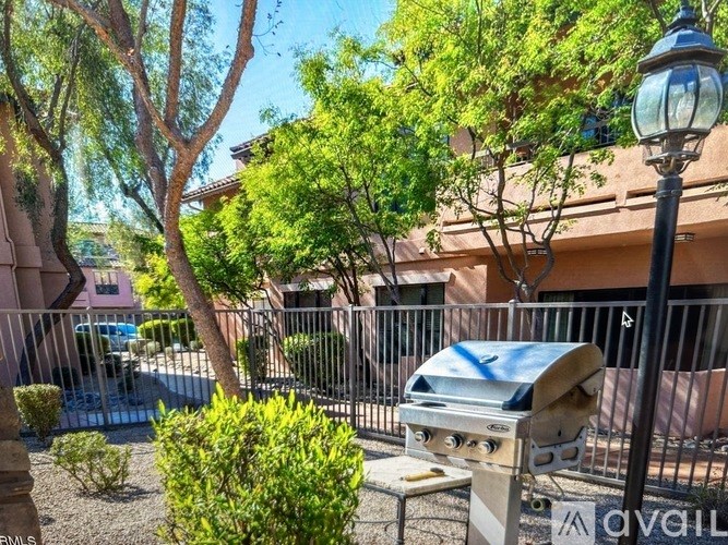 A barbecue grill is in the foreground of a residential area with trees and a fence.