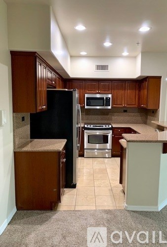 A kitchen with a black refrigerator, stainless steel oven, and microwave.