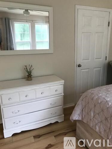 A white dresser with a mirror above it and a bed with a pink comforter to the right.