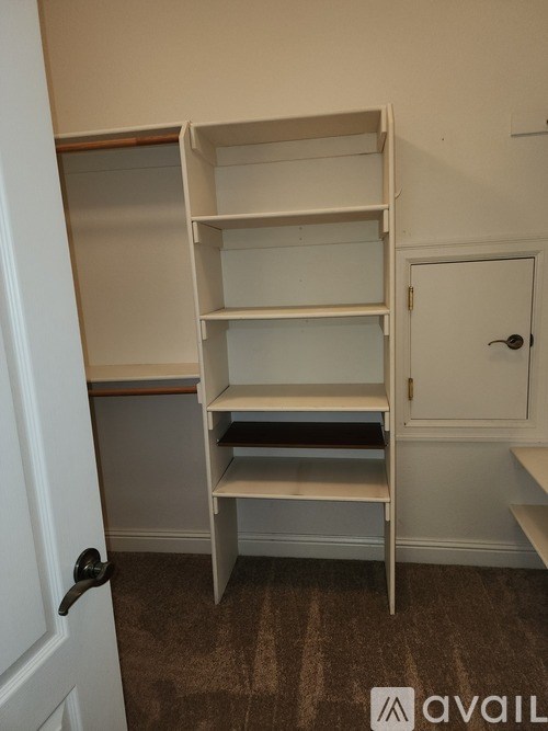 A white shelving unit with four shelves is in a room with a white door.