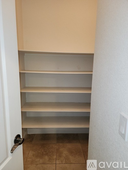 A white door with a silver handle is open to a hallway with a white wall and a tiled floor.