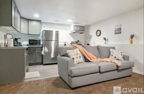 A living room with a grey couch and a kitchen area in the background.