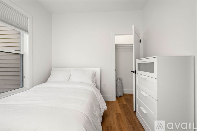 A white bedroom with a bed, nightstand, and a window with blinds.
