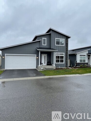 A grey house with a white garage door is in front of a cloudy sky.