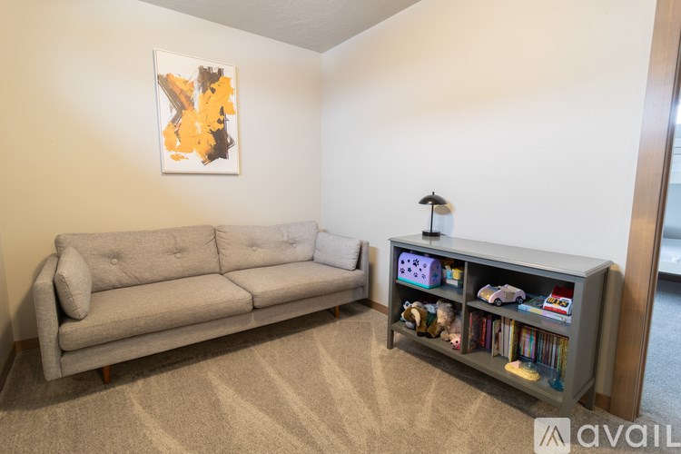 A living room with a grey couch and a bookshelf filled with books and toys.