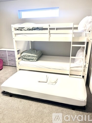 A white bunk bed with a mattress and a pull-out mattress in a room.