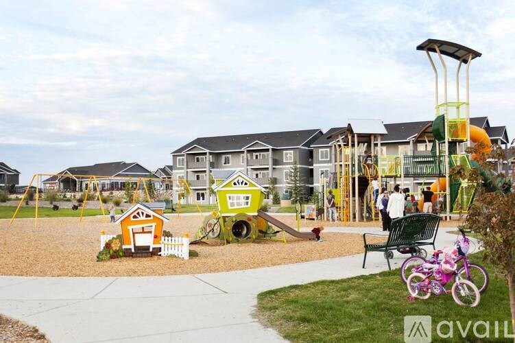 A playground with a slide, swings, and a sandbox in front of a row of houses.
