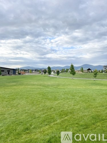 A grassy field with a cloudy sky and some buildings in the distance.