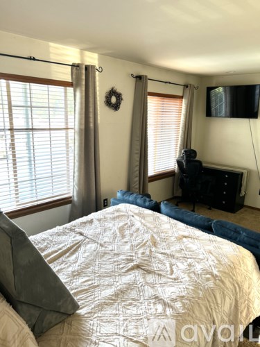A bedroom with a bed, a TV, and a window with blinds.