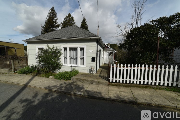 A small white house with a black roof and a white picket fence.