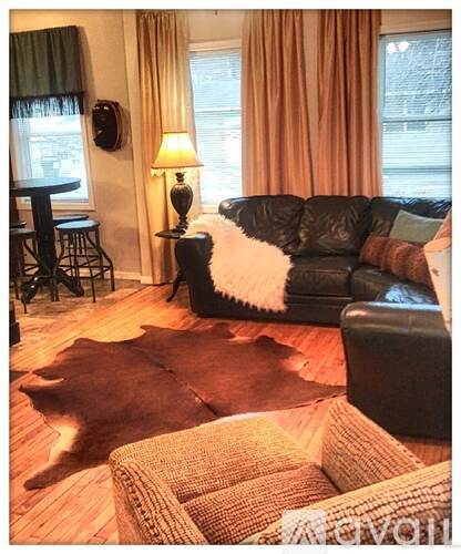 A living room with a black leather couch and a brown cowhide rug.