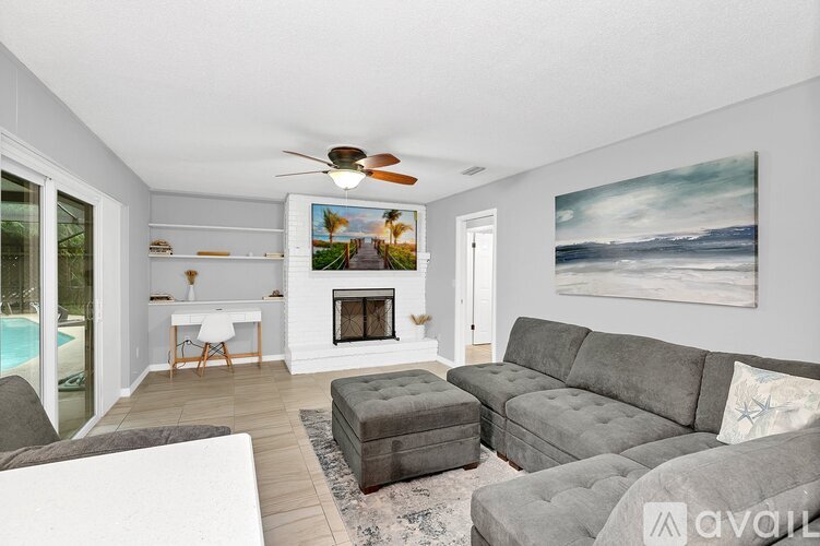 A living room with a grey couch, a fireplace, and a painting of a beach scene on the wall.