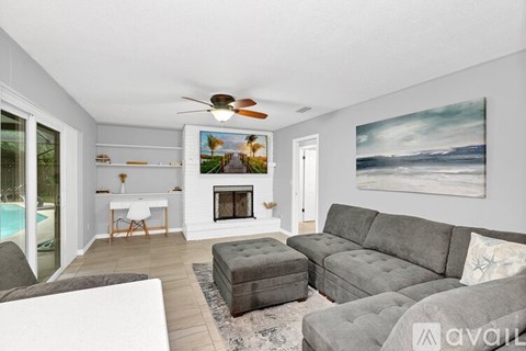 A living room with a grey couch, a fireplace, and a painting of a beach scene on the wall.
