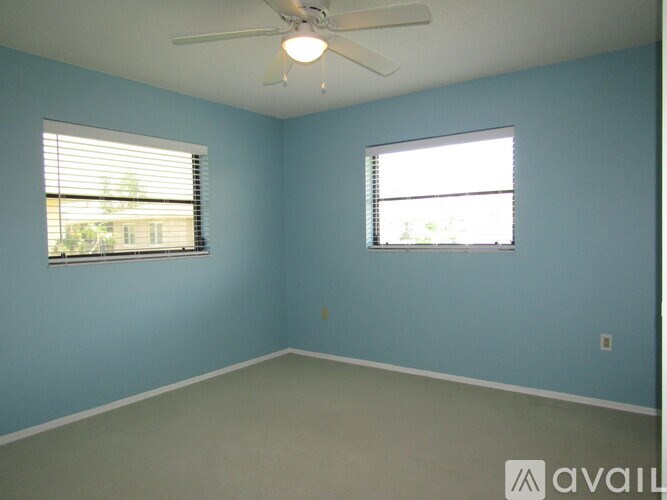 A room with a ceiling fan and two windows.