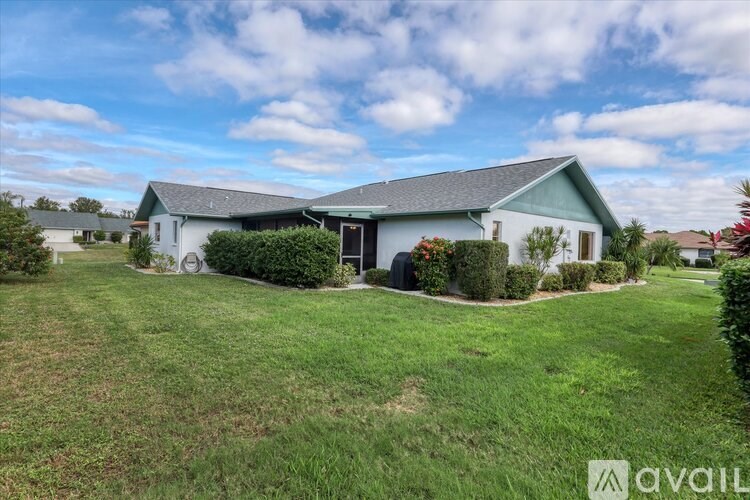 A house with a green roof and a white exterior is surrounded by a well-maintained lawn.