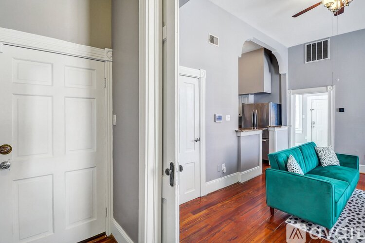 A green couch with white pillows is in the middle of a room with a white door and a white wall.
