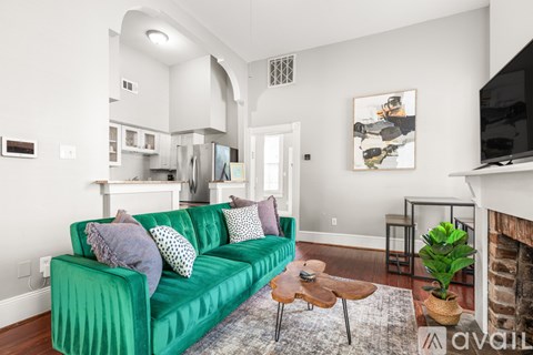 A green couch with white pillows is in the middle of a room with a white door and a white wall.