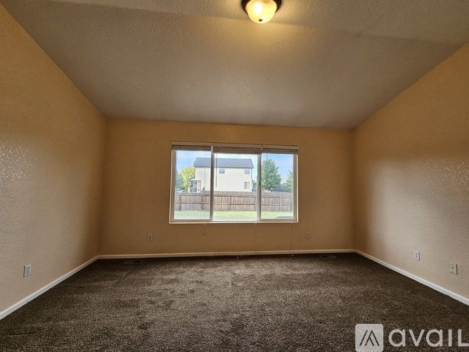 A room with a carpeted floor and a window overlooking a fence.