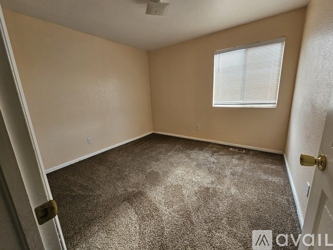 A room with a carpeted floor, a window with blinds, and a door with a lock.