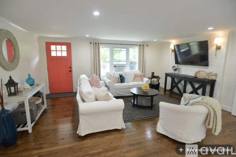 A living room with white furniture and a red door.