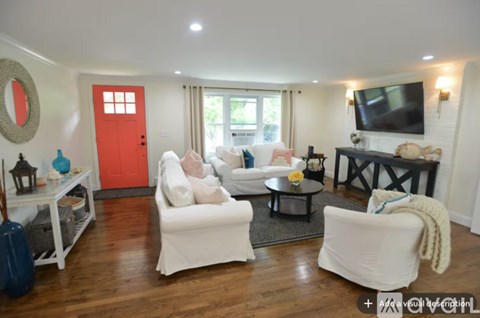 A living room with white furniture and a red door.
