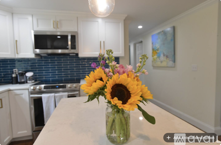 A vase with sunflowers and other flowers sits on a kitchen counter.