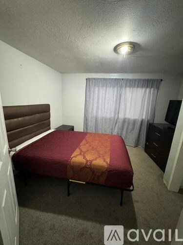 A bedroom with a bed, dresser, and window with curtains.