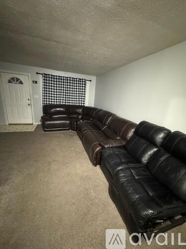 A black leather couch in a room with a door and window.