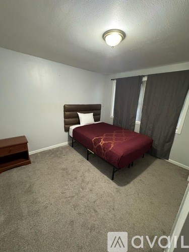 A bedroom with a bed, nightstand, and window with curtains.