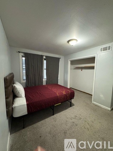 A bedroom with a red bedspread and a brown headboard.