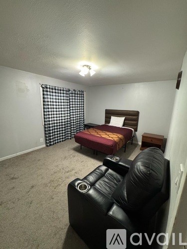 A black leather couch sits in a room with a bed and a small table.