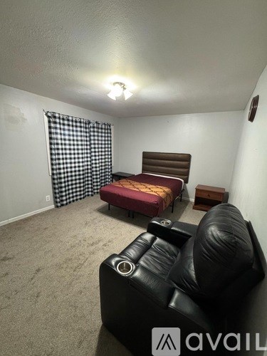 A black leather couch sits in a room with a checkered curtain and a bed with a red headboard.