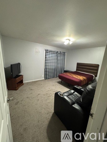 A living room with a black leather couch and a television on a wooden stand.