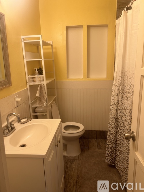 A bathroom with yellow walls has a white sink, toilet, and a shower with a curtain.