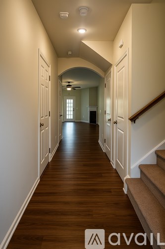A long hallway with a staircase on the right and a light at the end.