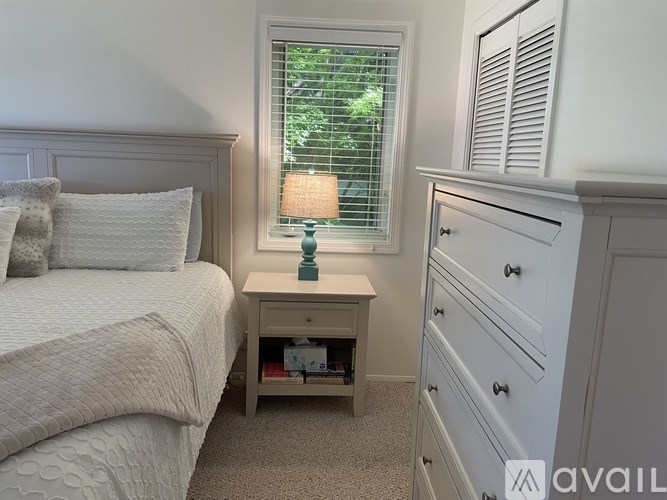 A bedroom with a bed, nightstand, and a window with blinds.